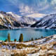 Alpine lake with turquoise water surrounded by snow-covered mountains and evergreen forests in Kazakhstan